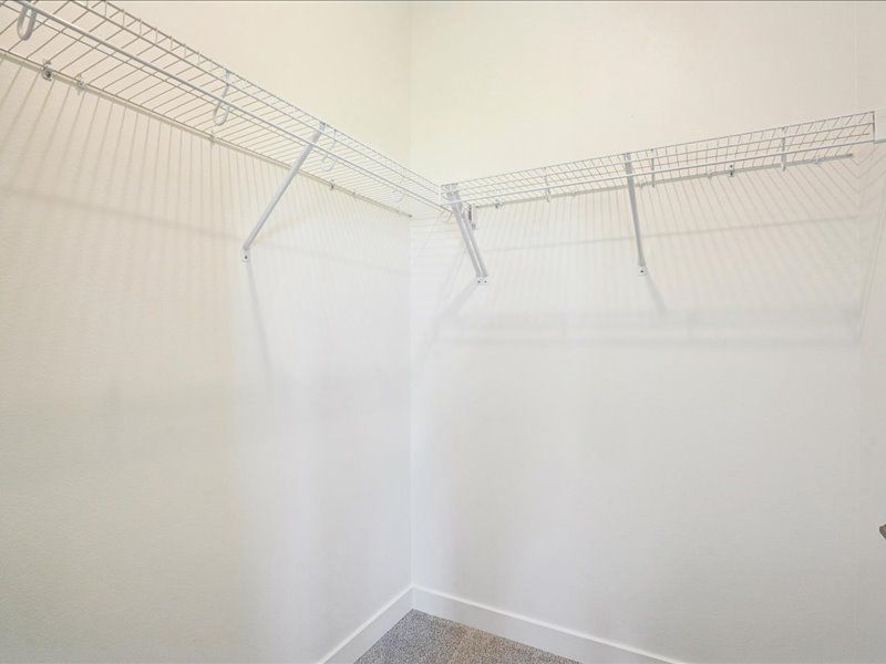Empty white closet with wire shelving along two walls and a tiled floor