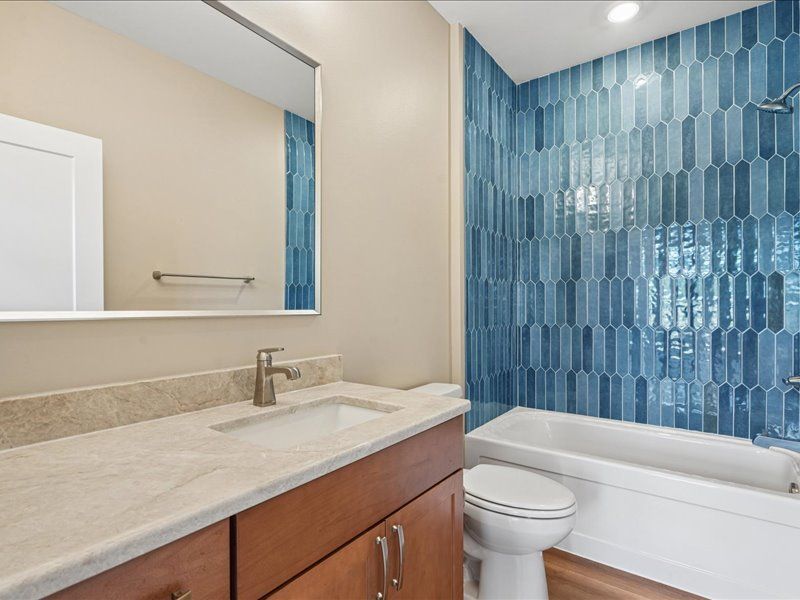 Modern bathroom with beige vanity, large mirror, and blue tiled shower surround beside a white tub and toilet