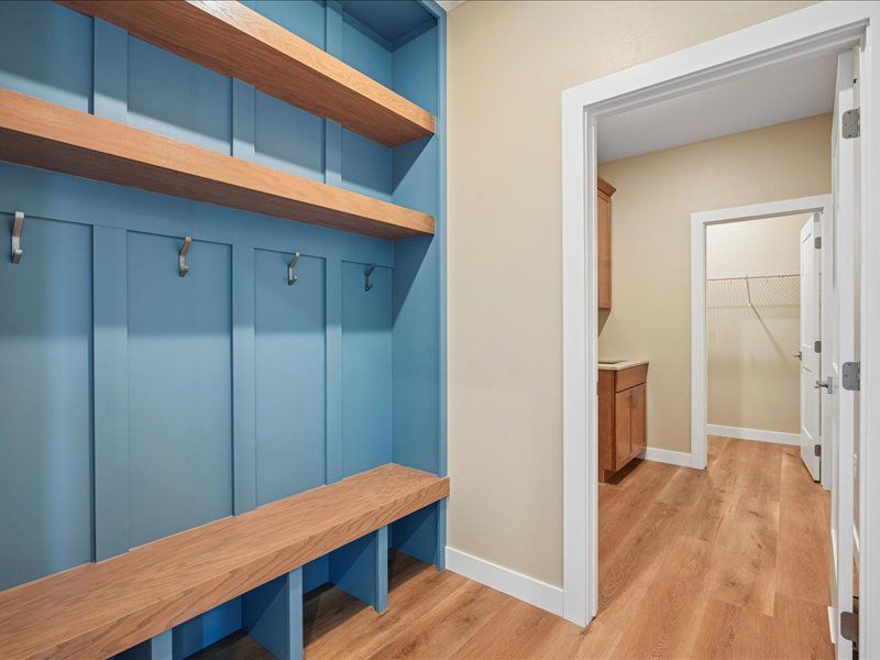Blue mudroom lockers with wooden bench and shelves, opening to a hardwood-floored hallway.