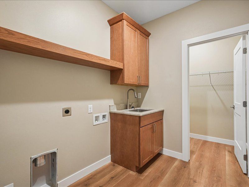 Empty laundry room with wood shelves, cabinet sink, and doorway to a tiled shower area.