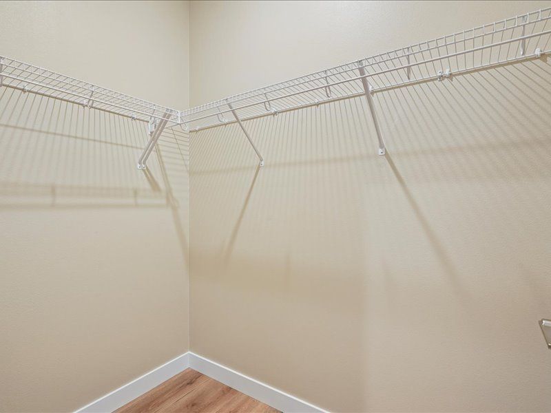 Empty beige closet with white wire shelving and carpeted floor corners