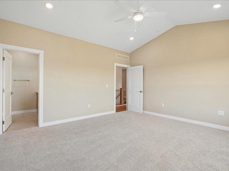 Empty beige bedroom with carpet, ceiling fan, and two open doorways