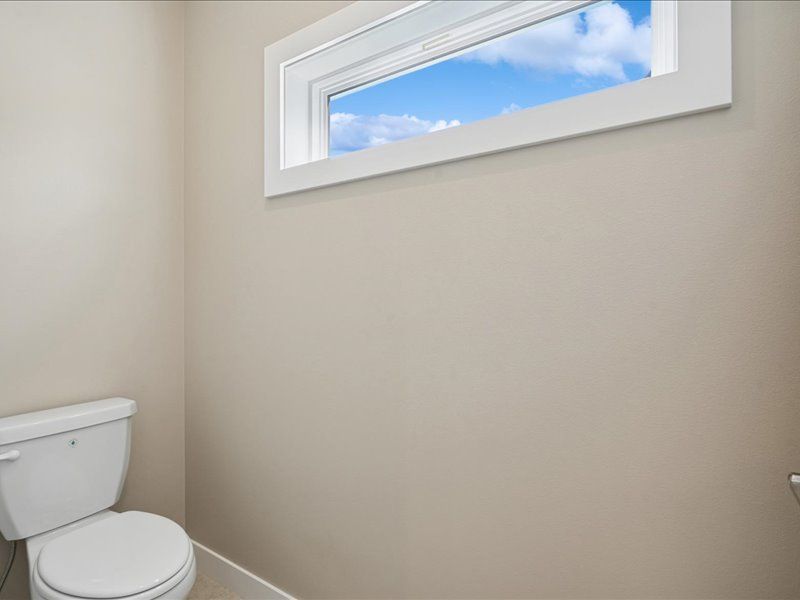 Small beige bathroom with a toilet and a narrow window showing blue sky.