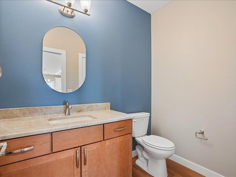 Bathroom with blue accent wall, wood vanity, oval mirror, and toilet.