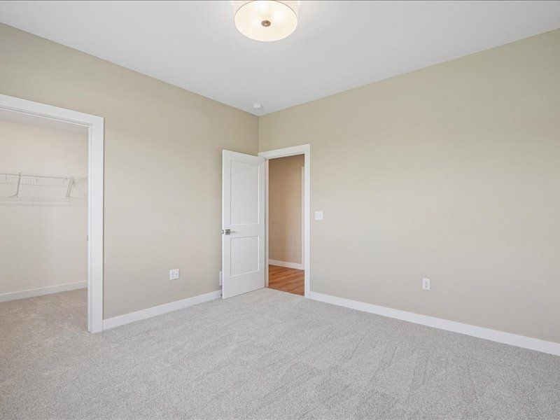 Empty beige bedroom with carpet, open white door, and closet opening.