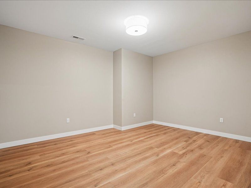 Empty beige room with wood flooring, white ceiling light, and gray walls