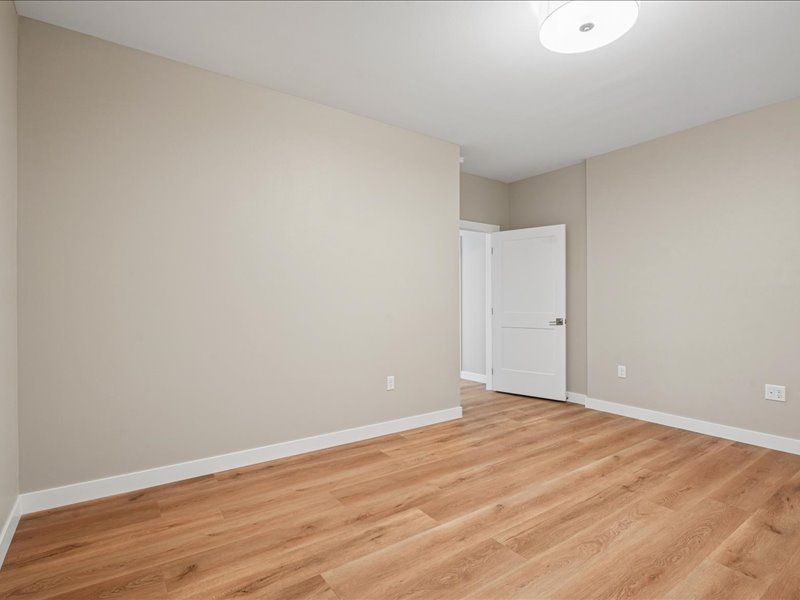 Empty beige bedroom with wood-look flooring and a white door.