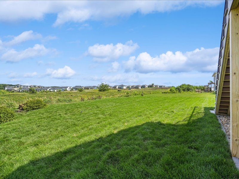 Grassy hillside beside a house under a blue sky with scattered clouds