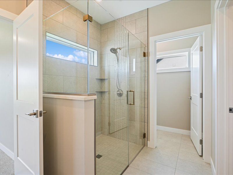 Modern beige-tiled bathroom with a glass walk-in shower and adjoining toilet area
