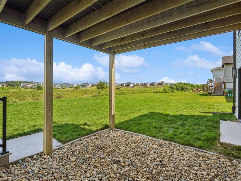 Covered patio with gravel floor overlooking a green backyard and distant houses on a sunny day