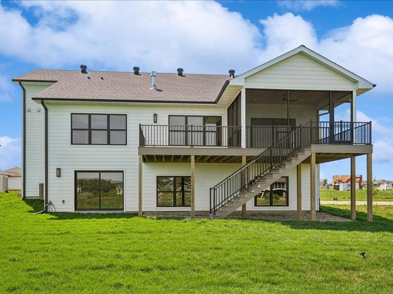 Two-story light gray house with a raised deck and exterior stairs over a grassy yard