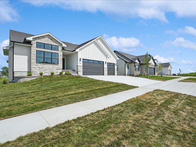 Suburban houses with attached garages along a sloped sidewalk and grassy lawn under a blue sky