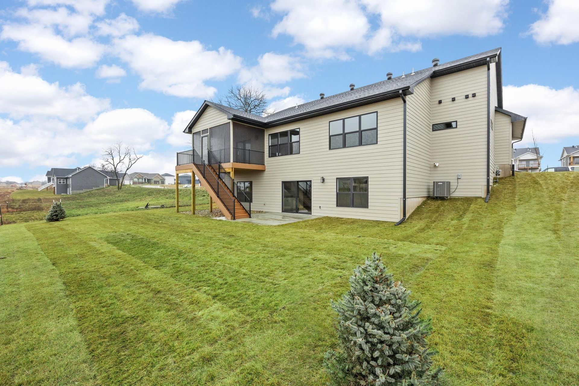A light tan two-story suburban house with a screened-in back deck and a sloped, freshly mowed grassy lawn.