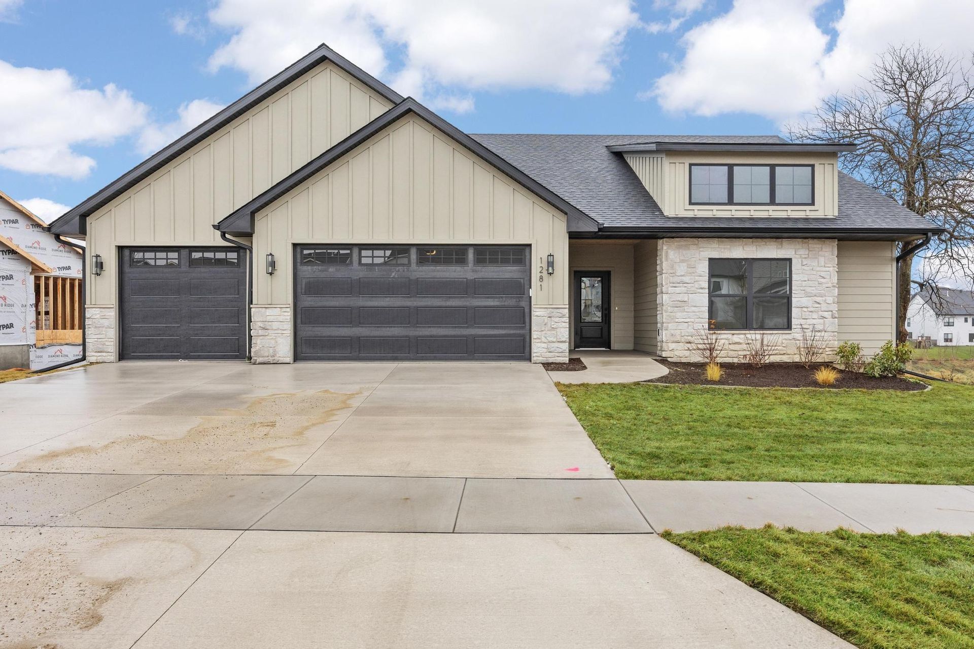 A modern single-story house with a three-car garage, stone and beige siding, a dark roof, and a front lawn.