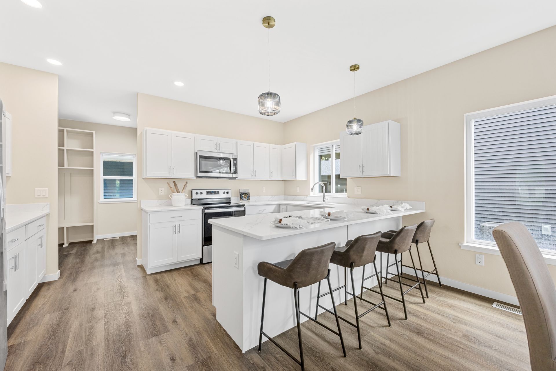 A bright, modern kitchen featuring white cabinets, a light-toned island with four gray bar stools, and wood-look flooring.