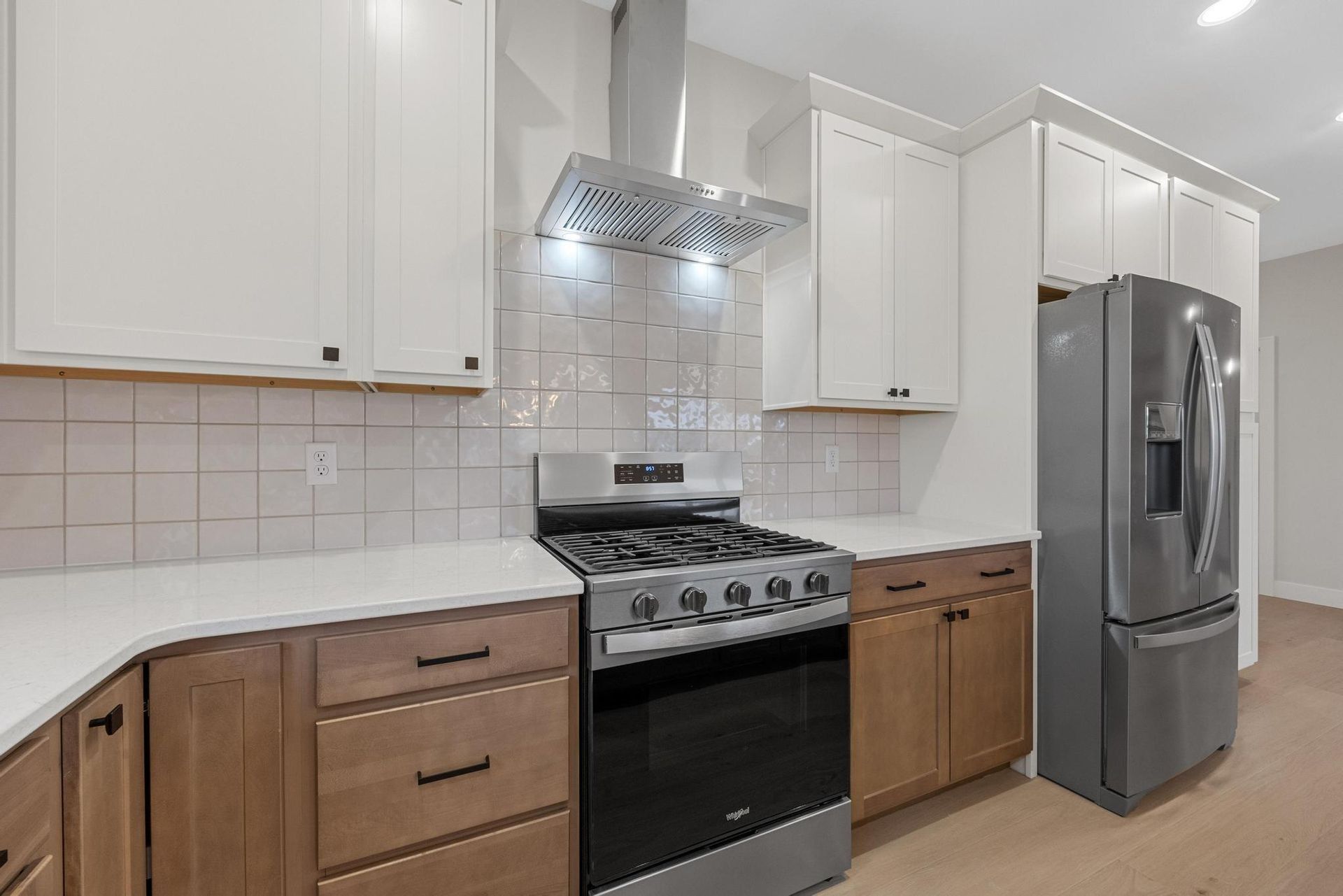 A modern kitchen featuring white upper cabinets, light wood lower cabinets, white countertops, and stainless appliances.