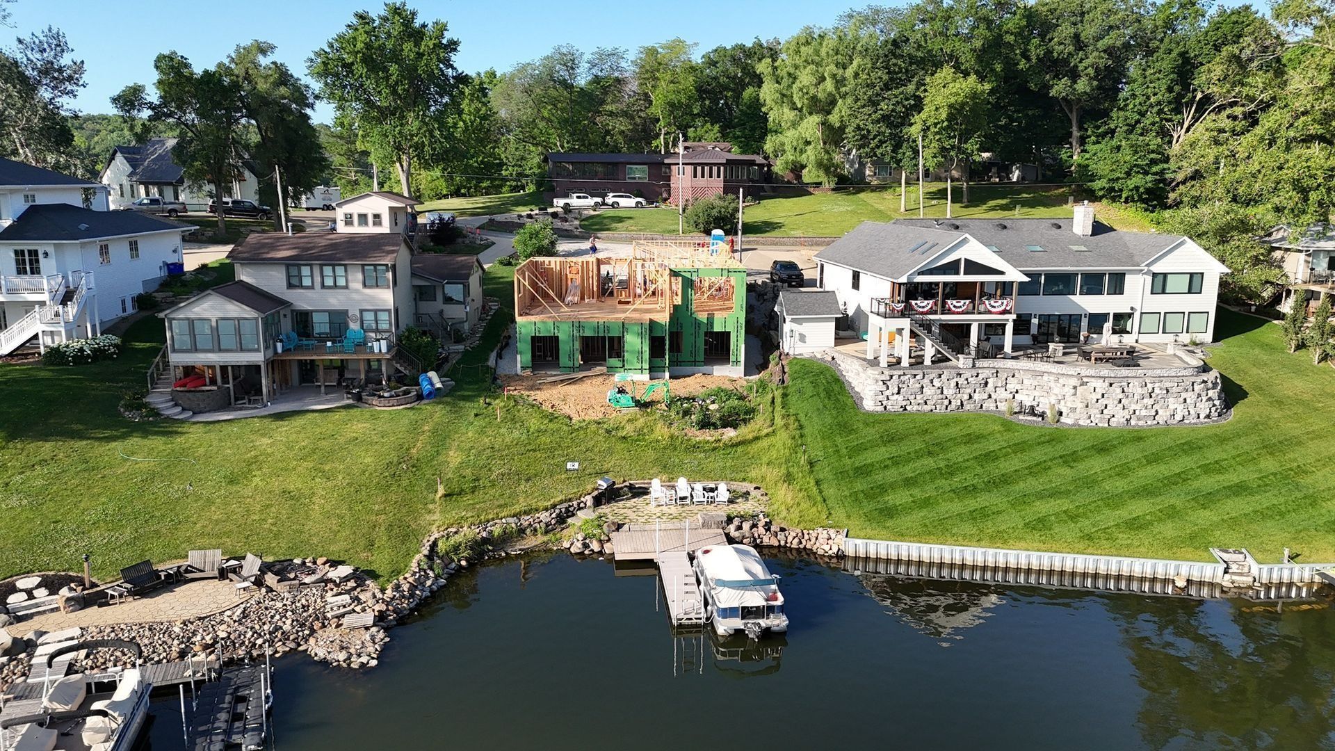 An aerial view of a lakeside property with a central house under construction, flanked by two finished homes and a dock.