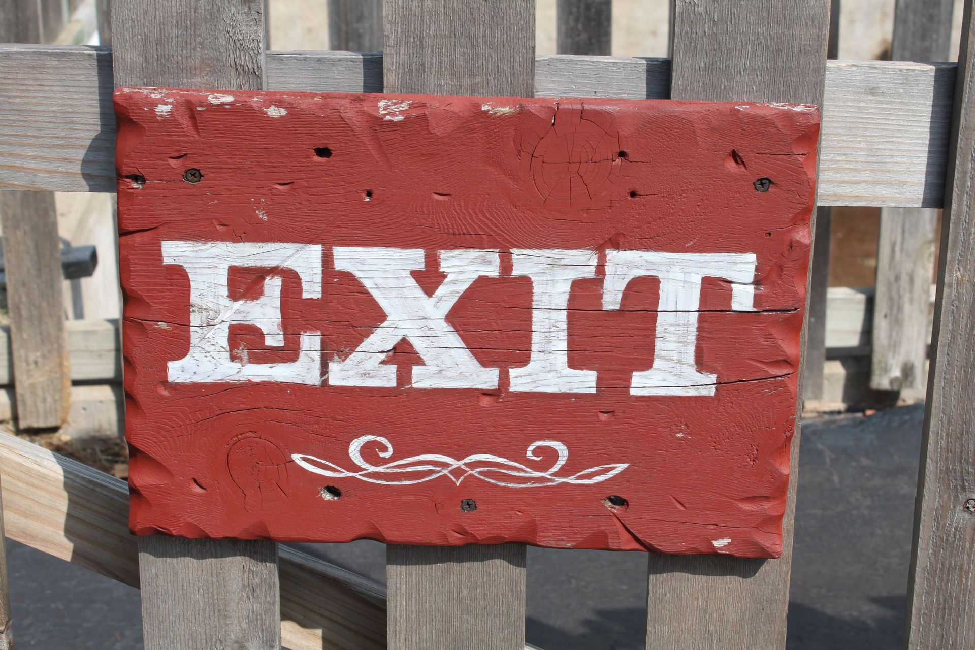 Red wooden sign with white “EXIT” text on a slatted fence background.