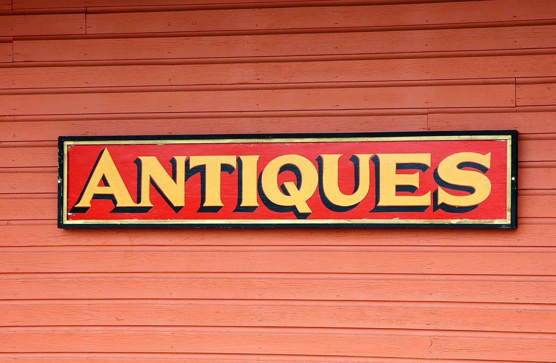 Red antique shop sign reading “ANTIQUES” on a weathered red wooden wall.