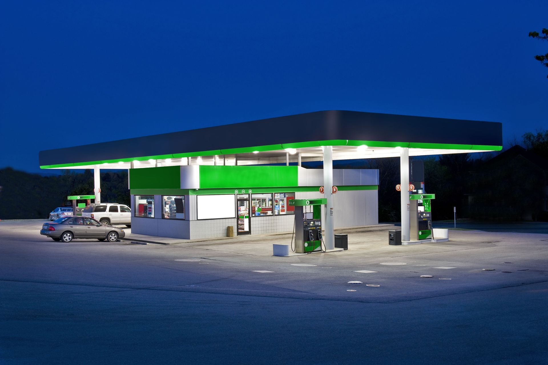 Gas station at dusk with green-and-white canopy and a few parked cars