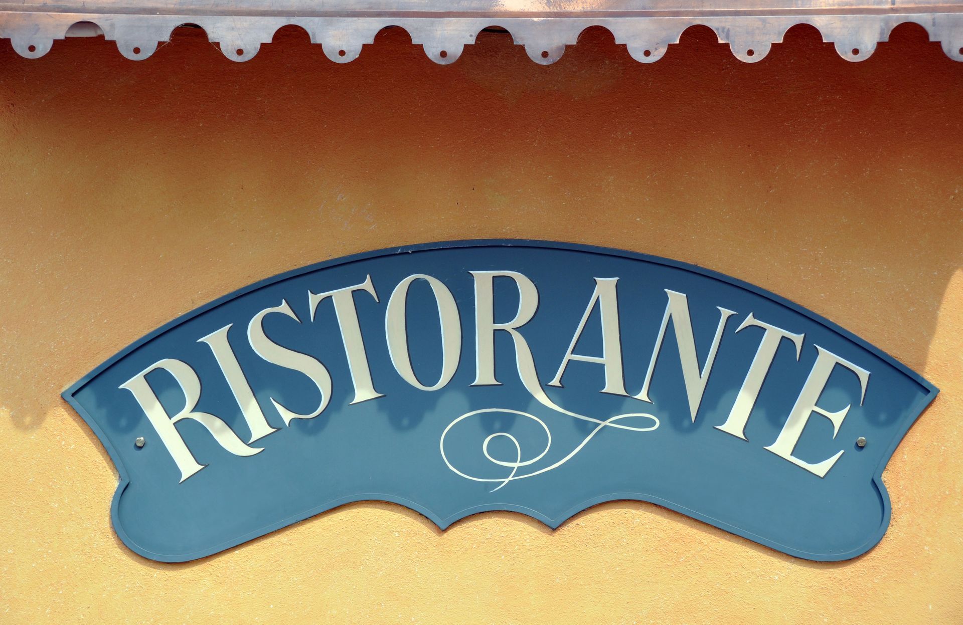 Blue “RISTORANTE” sign on a beige wall with decorative trim above