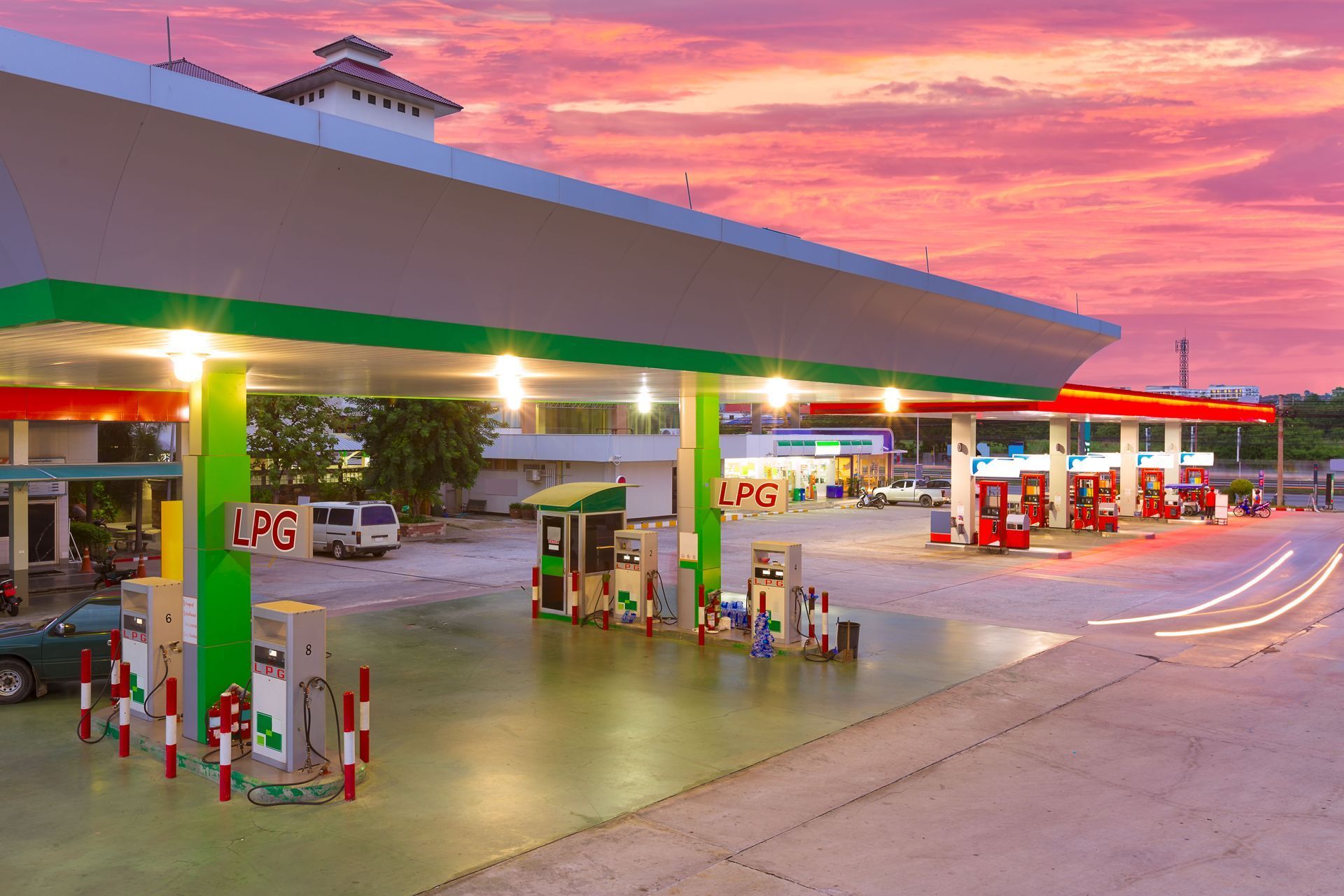 Gas station at dusk with green canopies, fuel pumps, and a pink-orange sunset sky