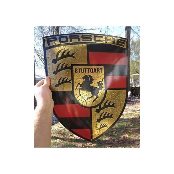 Hand holding a Porsche Stuttgart crest sign with gold, black, red, and a horse emblem outdoors