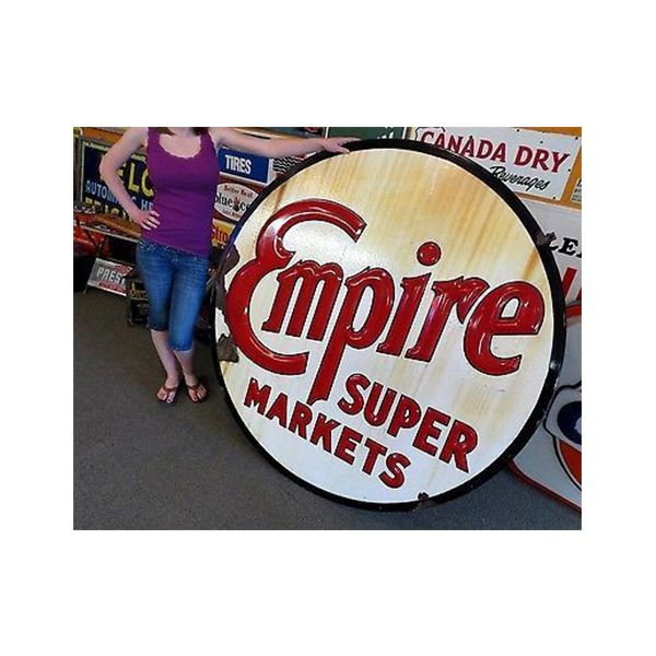 Woman standing beside a large circular Empire Super Markets sign indoors