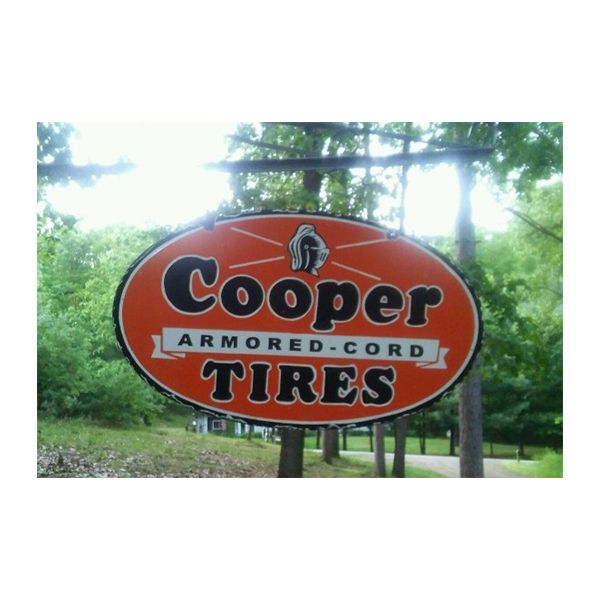 Cooper Tires oval sign on a roadside amid green trees
