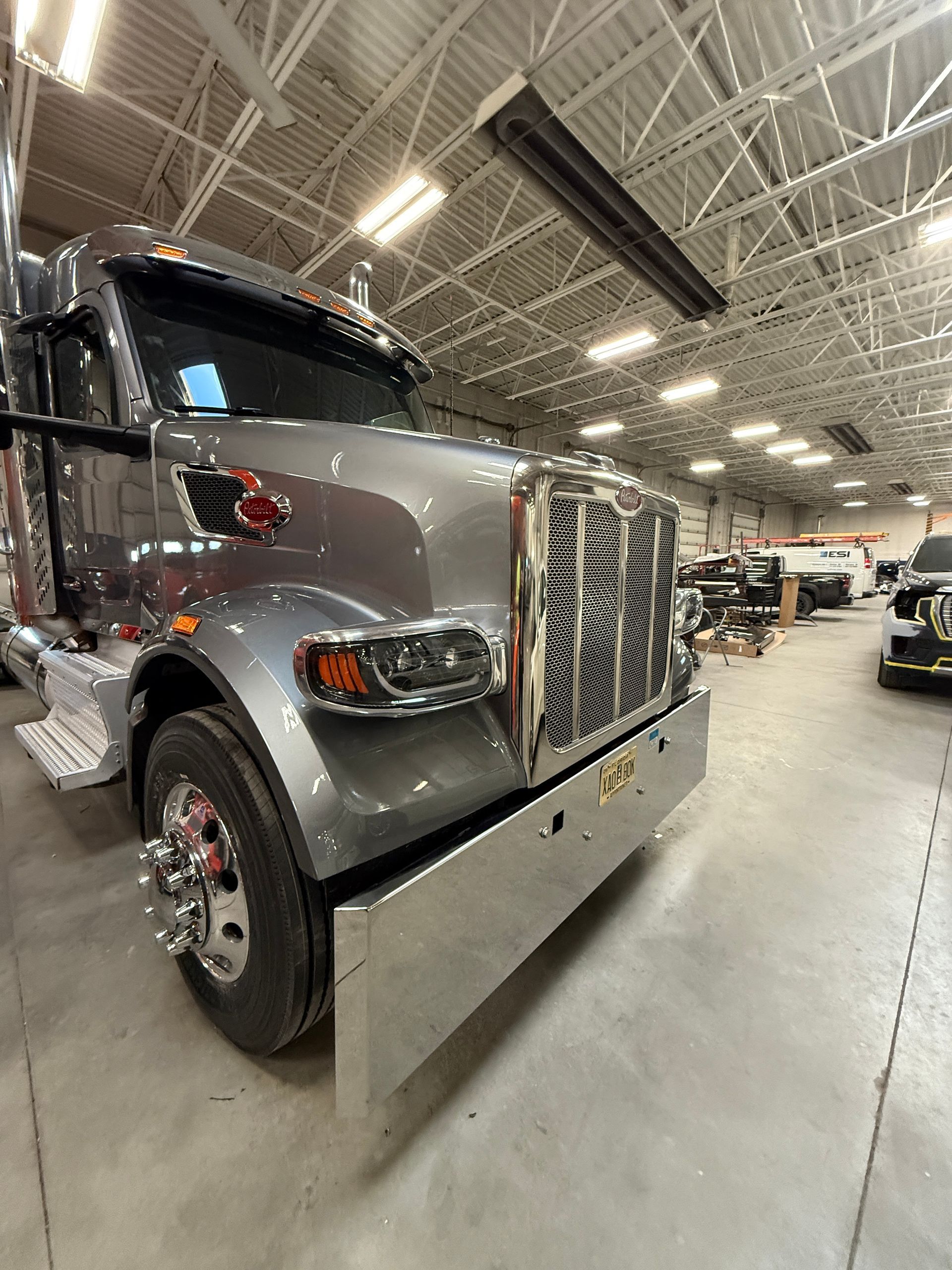 A low-angle view of a shiny grey Peterbilt semi-truck parked inside a well-lit industrial garage.