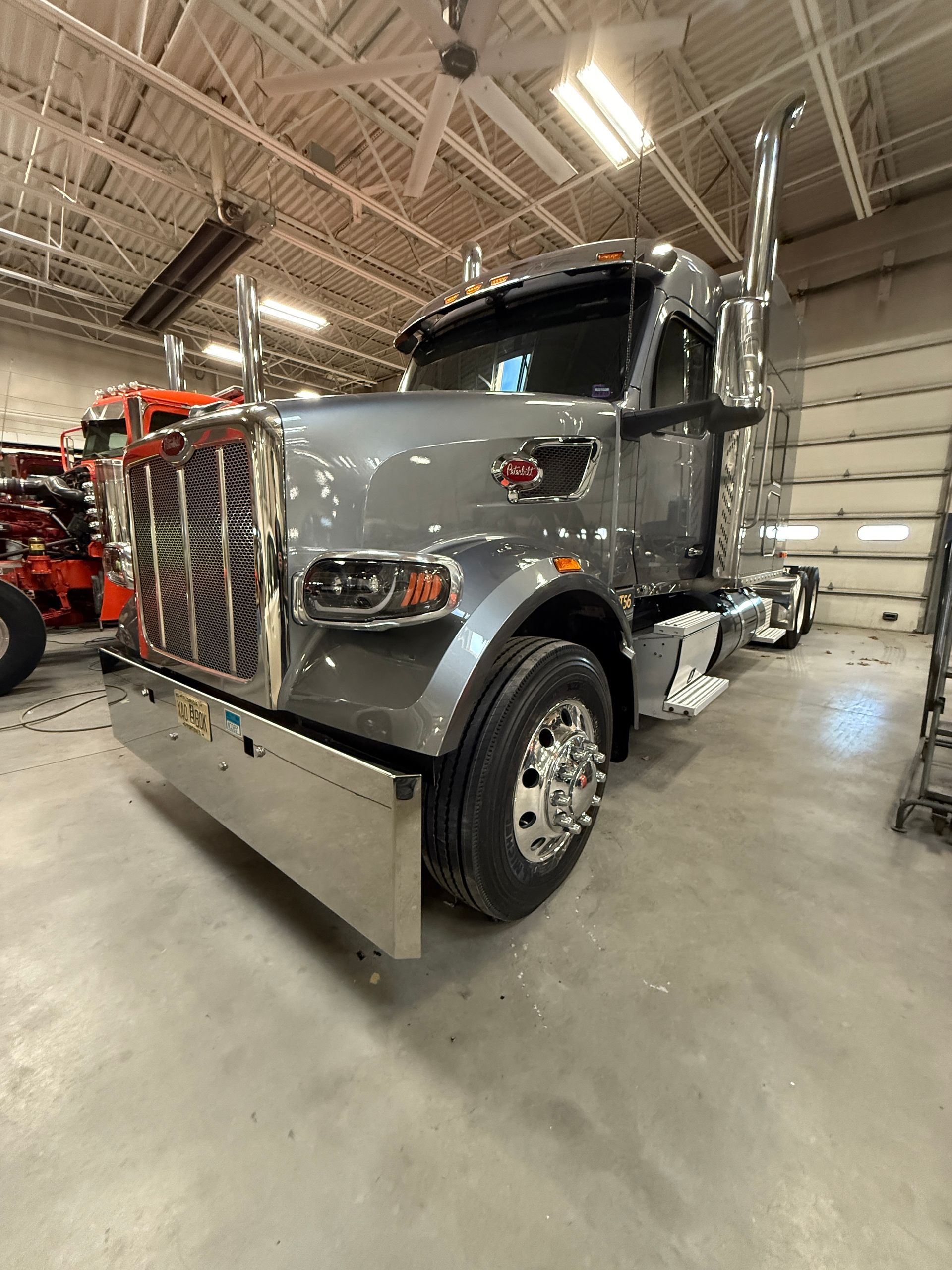 A metallic gray Peterbilt semi-truck parked inside a large, well-lit workshop with concrete floors.
