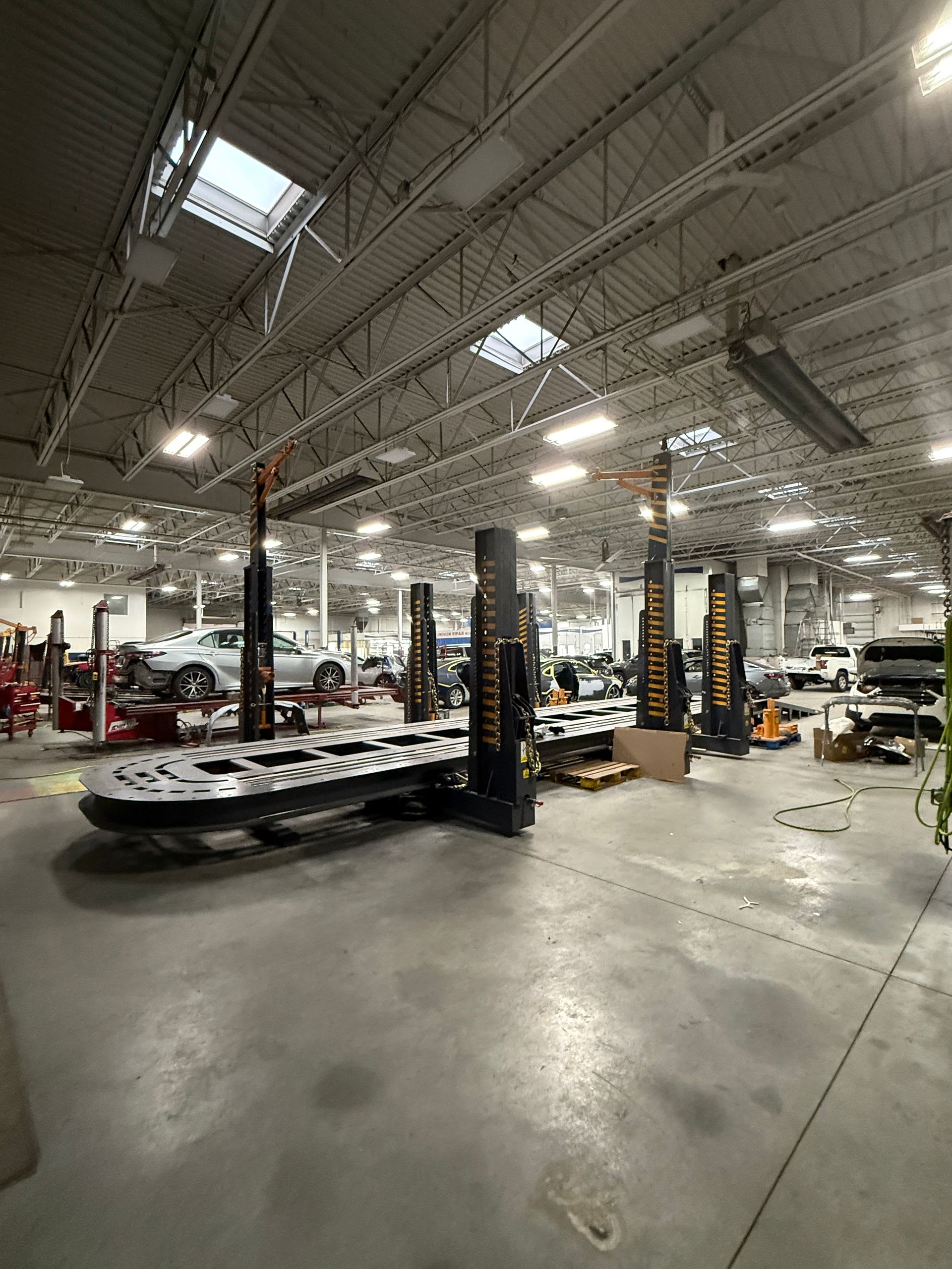 A large, industrial auto repair shop featuring multiple vehicle lifts with empty metal platforms and parked cars.