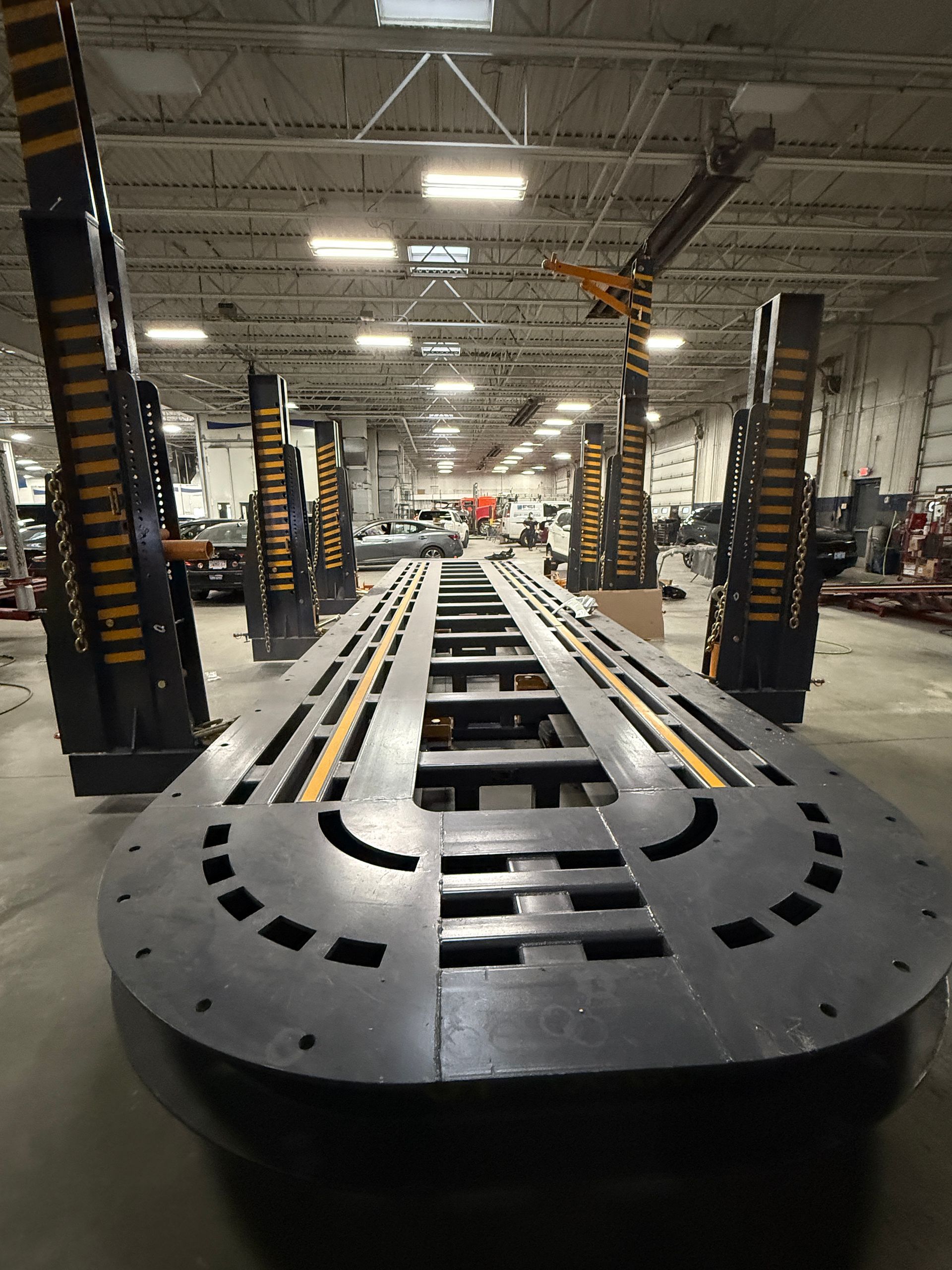 A long, U-shaped industrial metal frame sits in a workshop with several tall, yellow-striped support columns in the back.