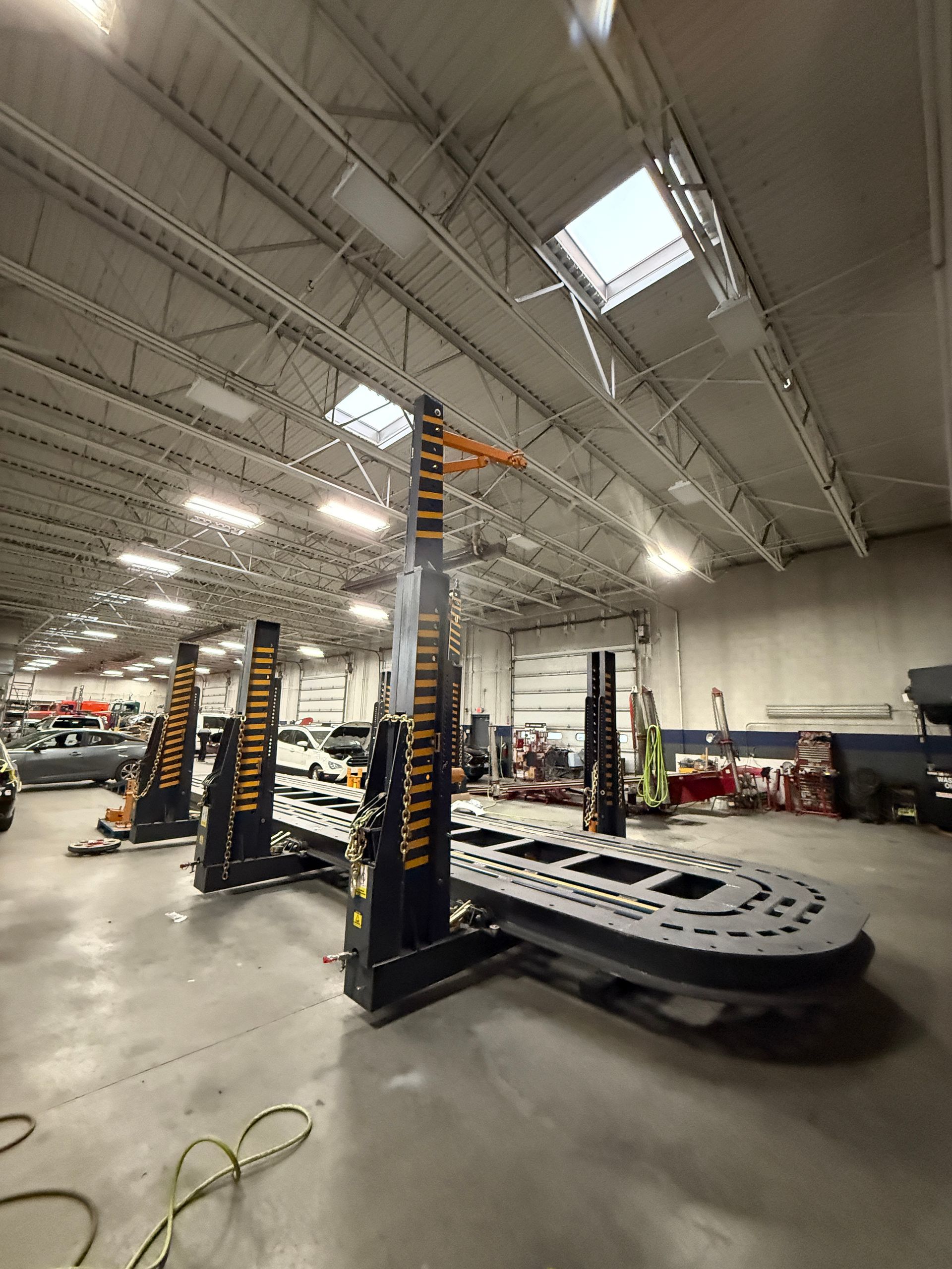 A wide-angle view of a professional auto body shop featuring black and yellow frame-straightening equipment on a floor.