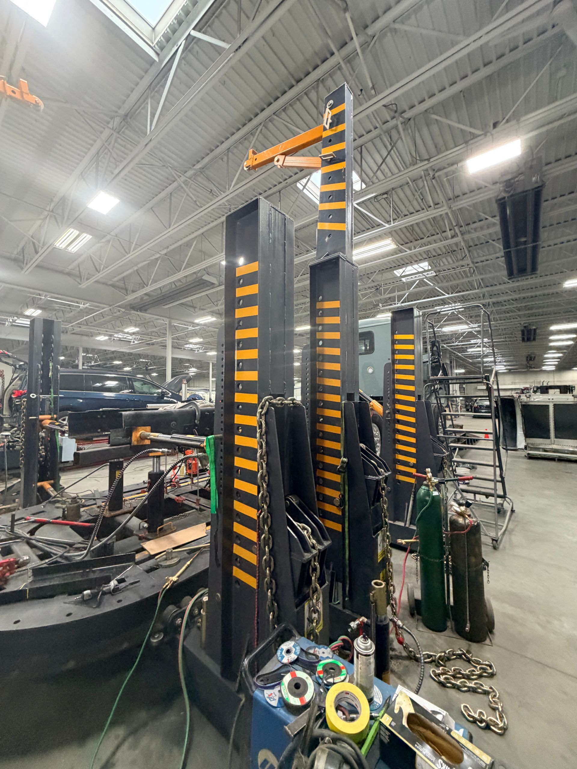 A row of heavy-duty auto body frame repair towers with yellow-and-black safety markings inside a spacious workshop.