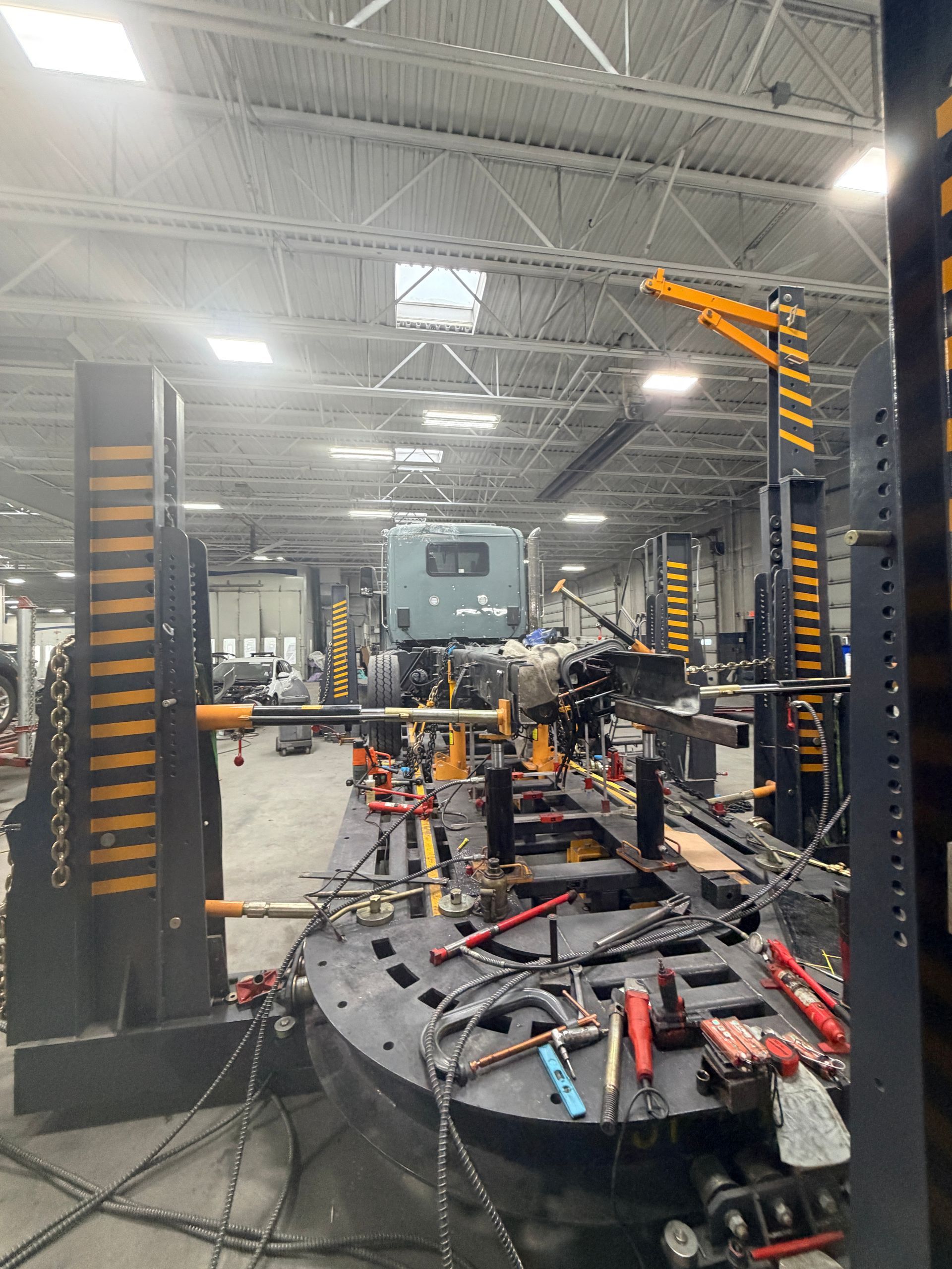 A large metal vehicle frame mounted on a black industrial repair rack inside a well-lit workshop.