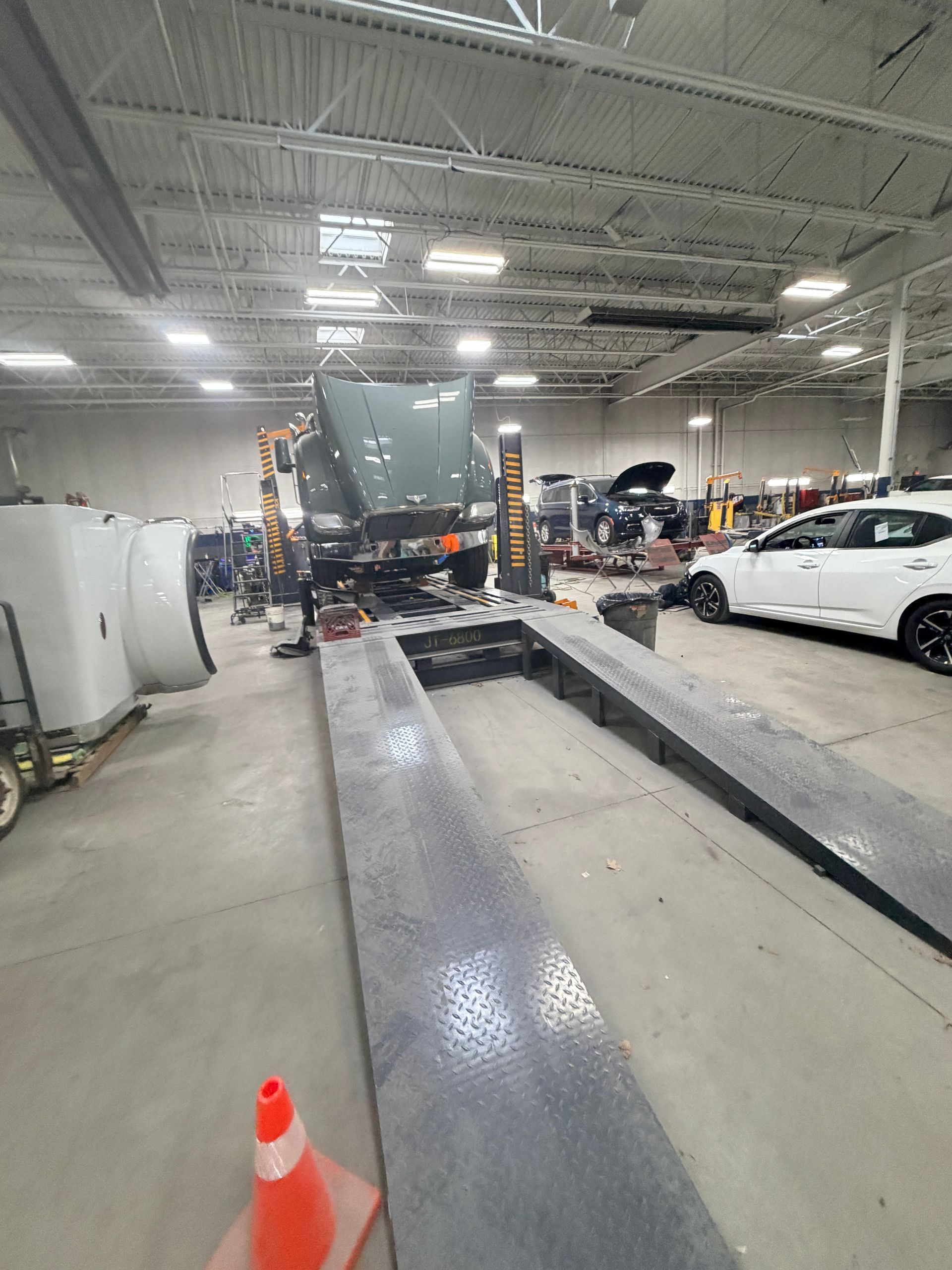 A high-angle view of a large automotive repair shop featuring a lifted dark semi-truck and a white car on the right.