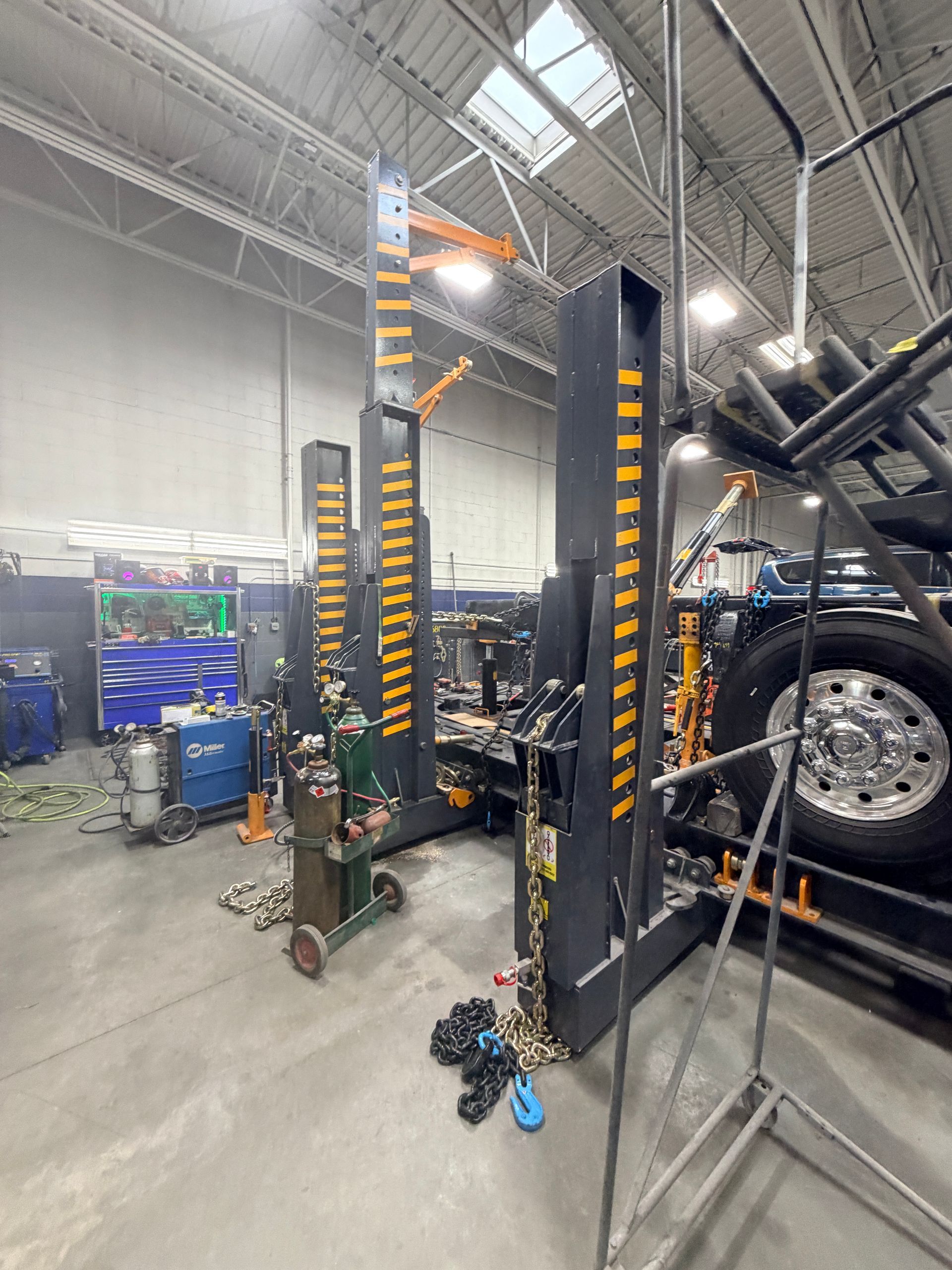 Two tall, black industrial collision repair towers stand on a workshop floor next to a truck wheel.