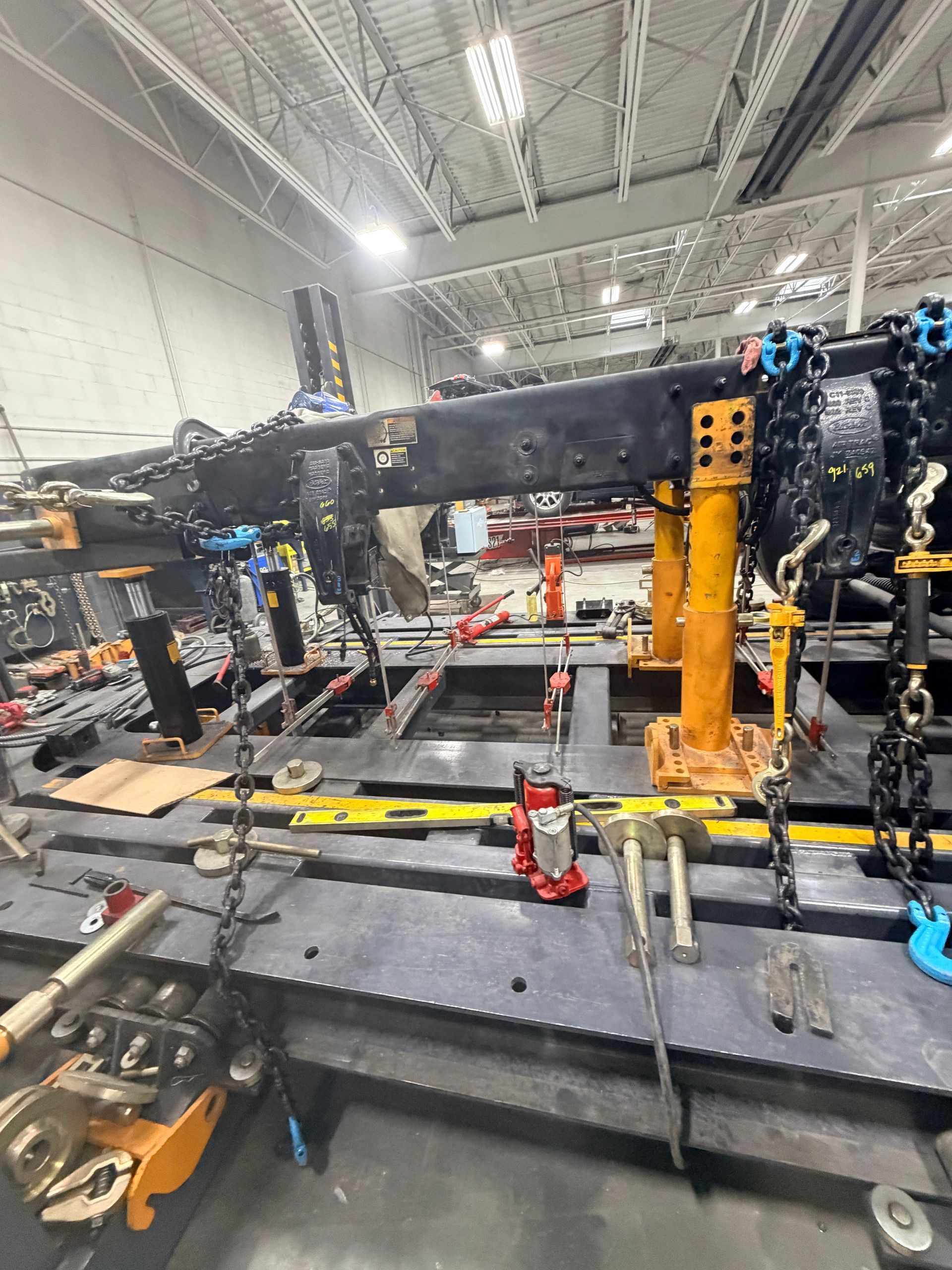 A heavy-duty frame alignment machine in a shop, featuring yellow metal supports, chains, and industrial tools.