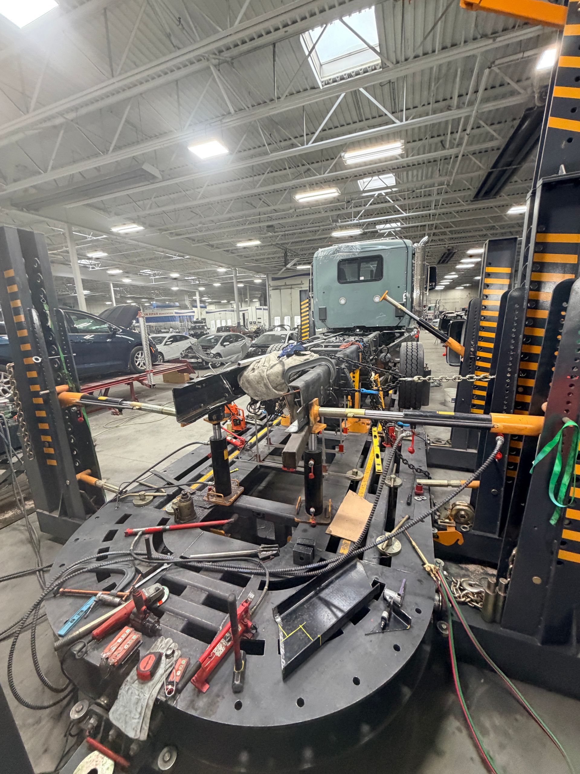 A heavy-duty truck cab mounted on a black frame in an industrial repair shop with various tools and equipment.