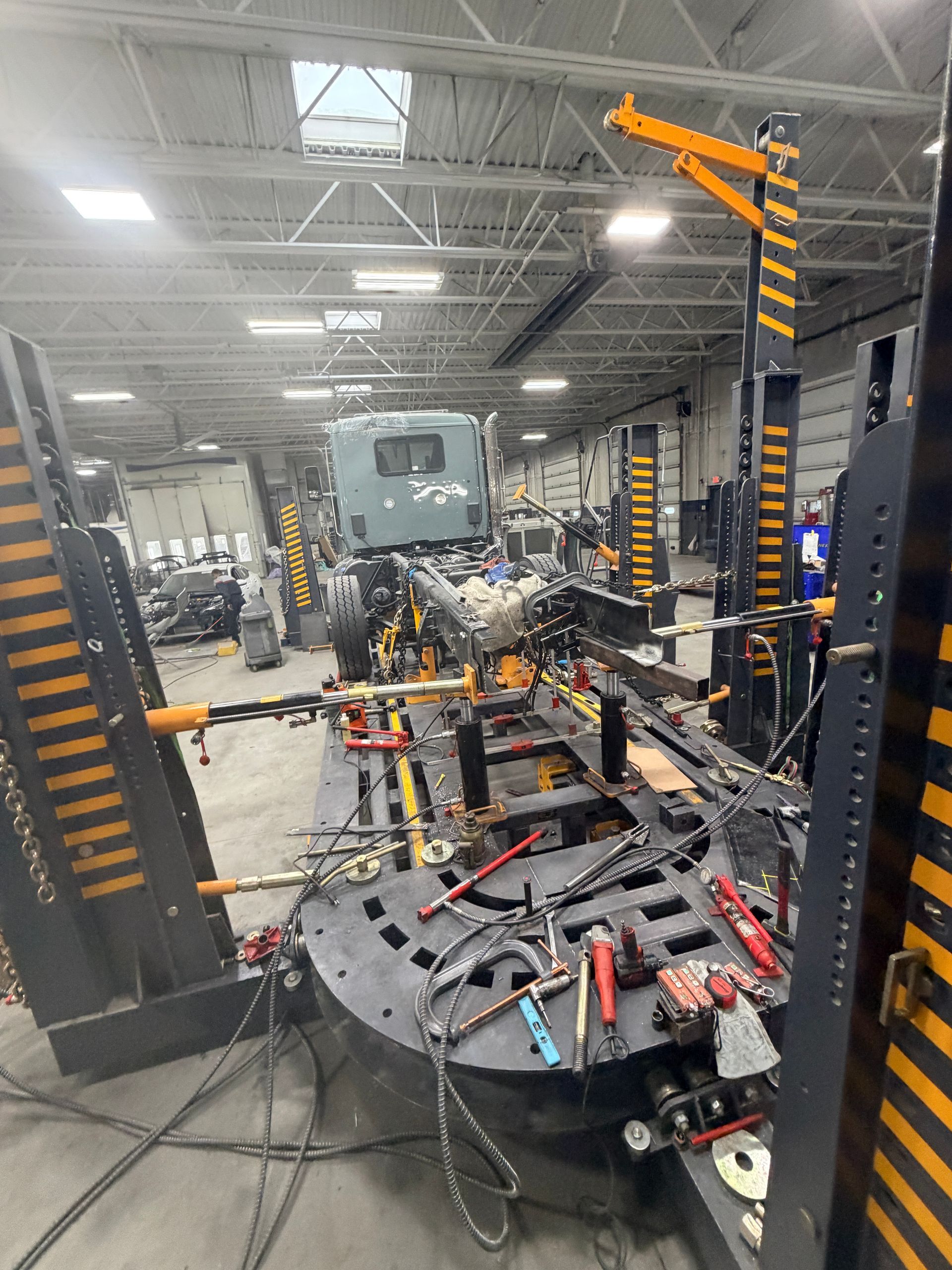 A semi-truck cabin and chassis secured on a heavy-duty frame rack inside an industrial repair shop.