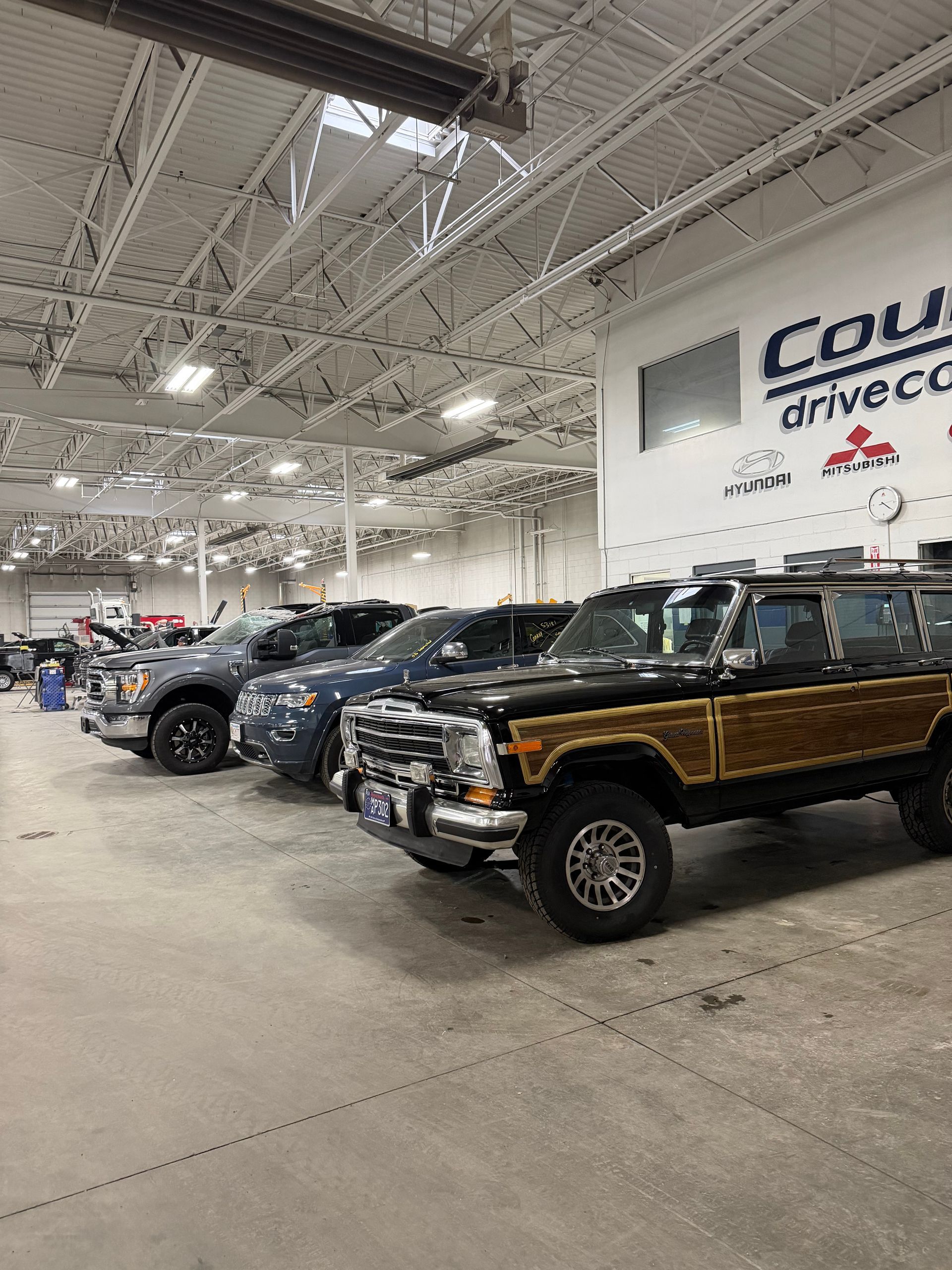 A row of parked vehicles, including a black SUV with wood-grain side paneling, inside a bright, high-ceilinged showroom.