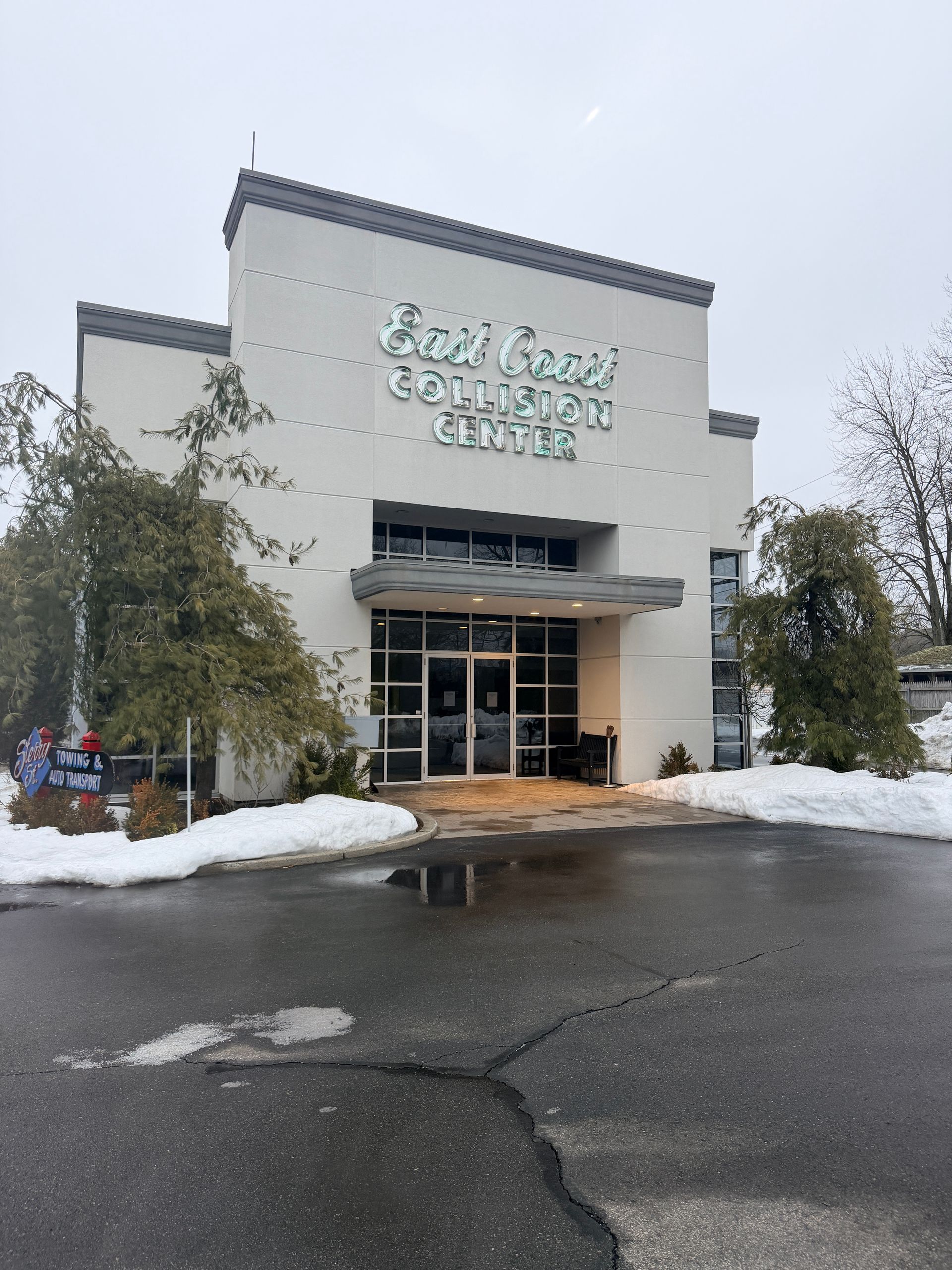 The East Coast Collision Center building with white stucco walls, glass entrance, and snow-covered ground in winter.
