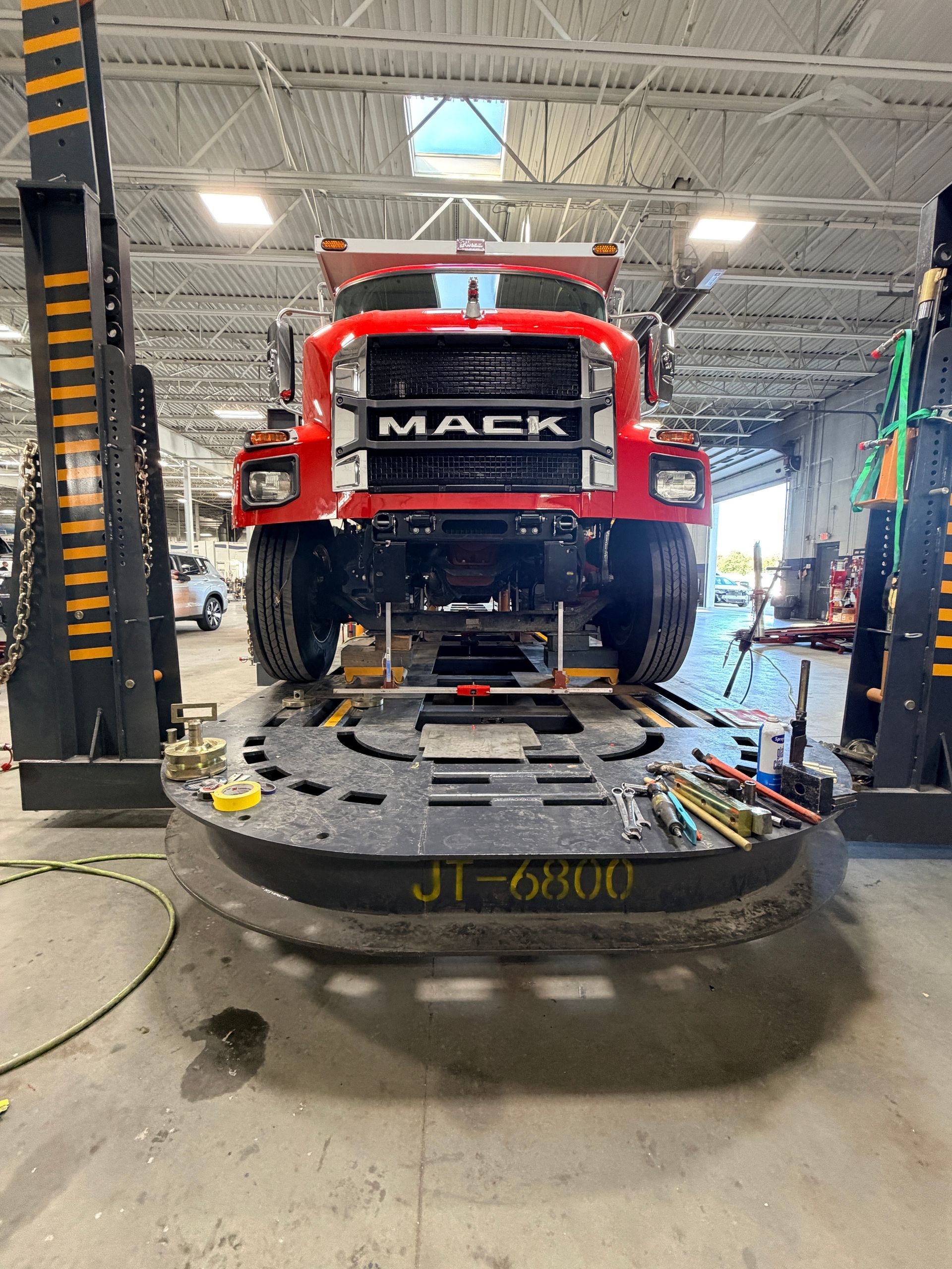 A bright red Mack truck positioned on an industrial lift inside a maintenance garage.