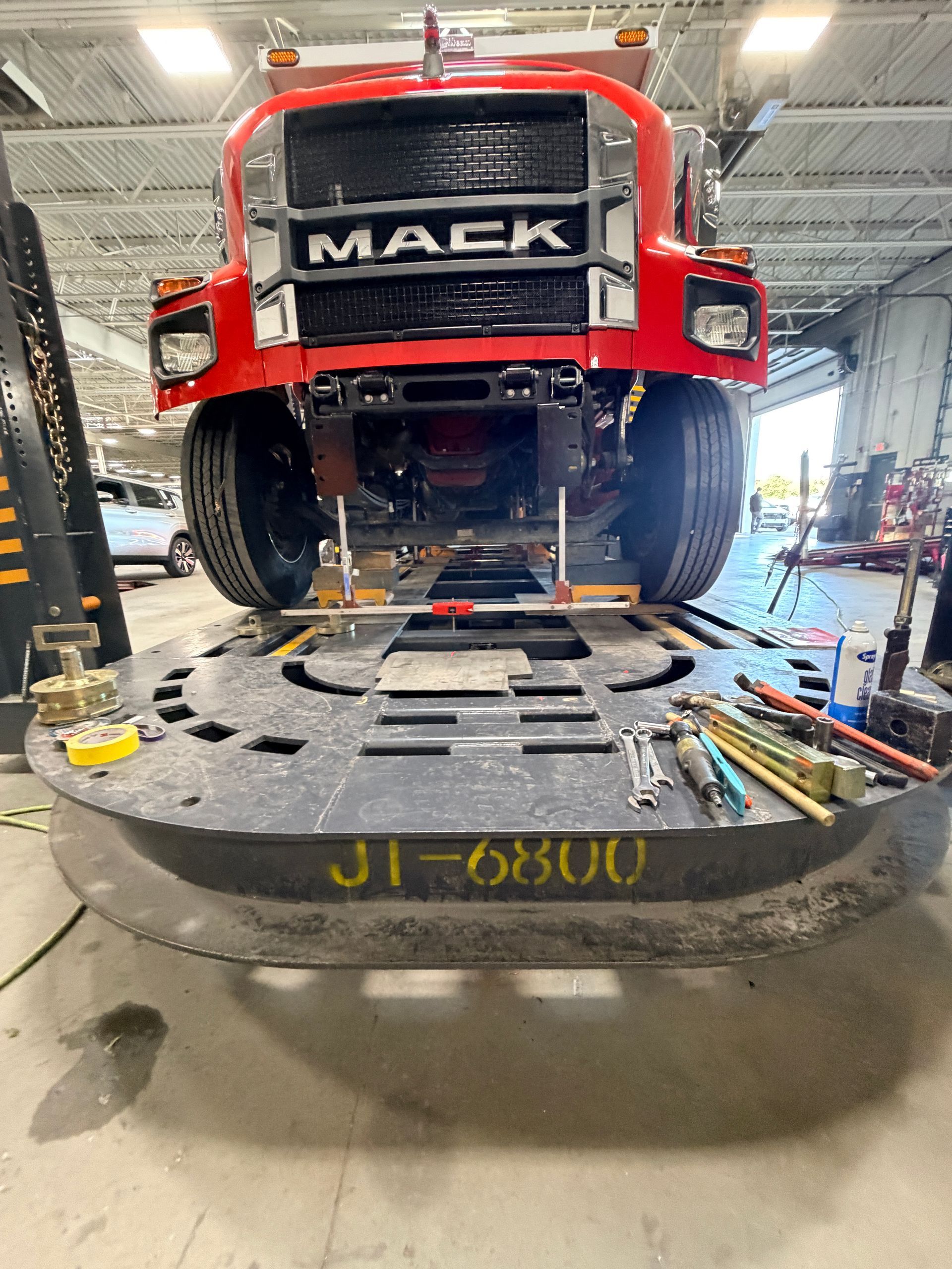 A red Mack truck sits on a large circular frame alignment machine in a workshop, with various tools laid on the platform.
