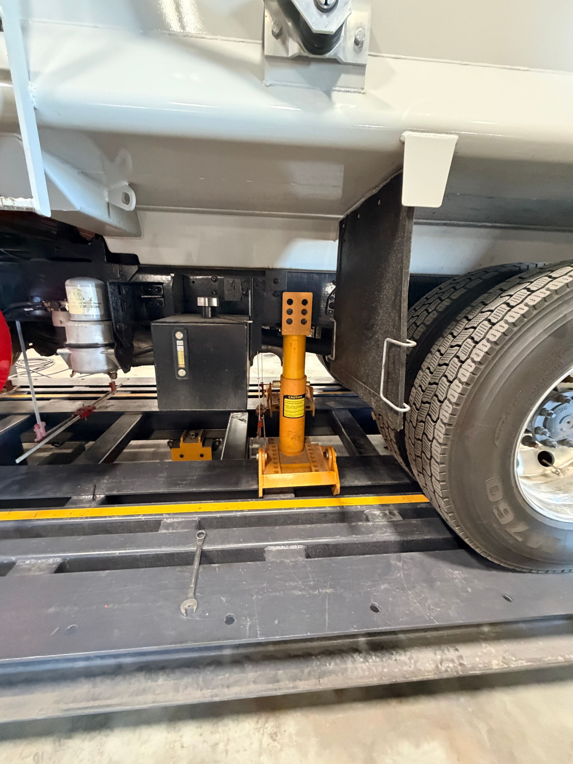 Yellow jack stand supporting the frame of a white commercial truck parked on a shop floor.