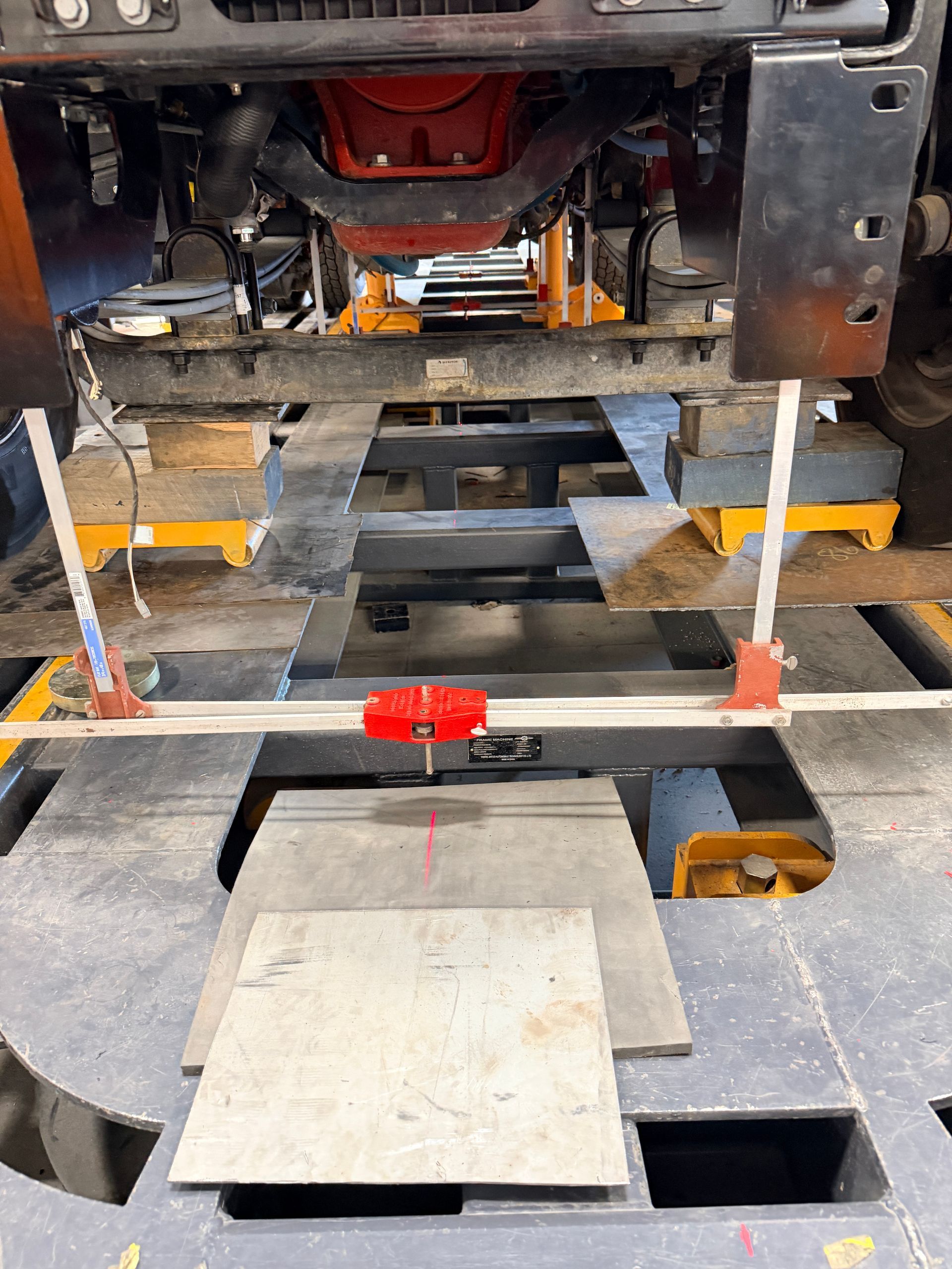 A red laser leveling tool is mounted on a bar attached to the front of a vehicle elevated on a service lift.