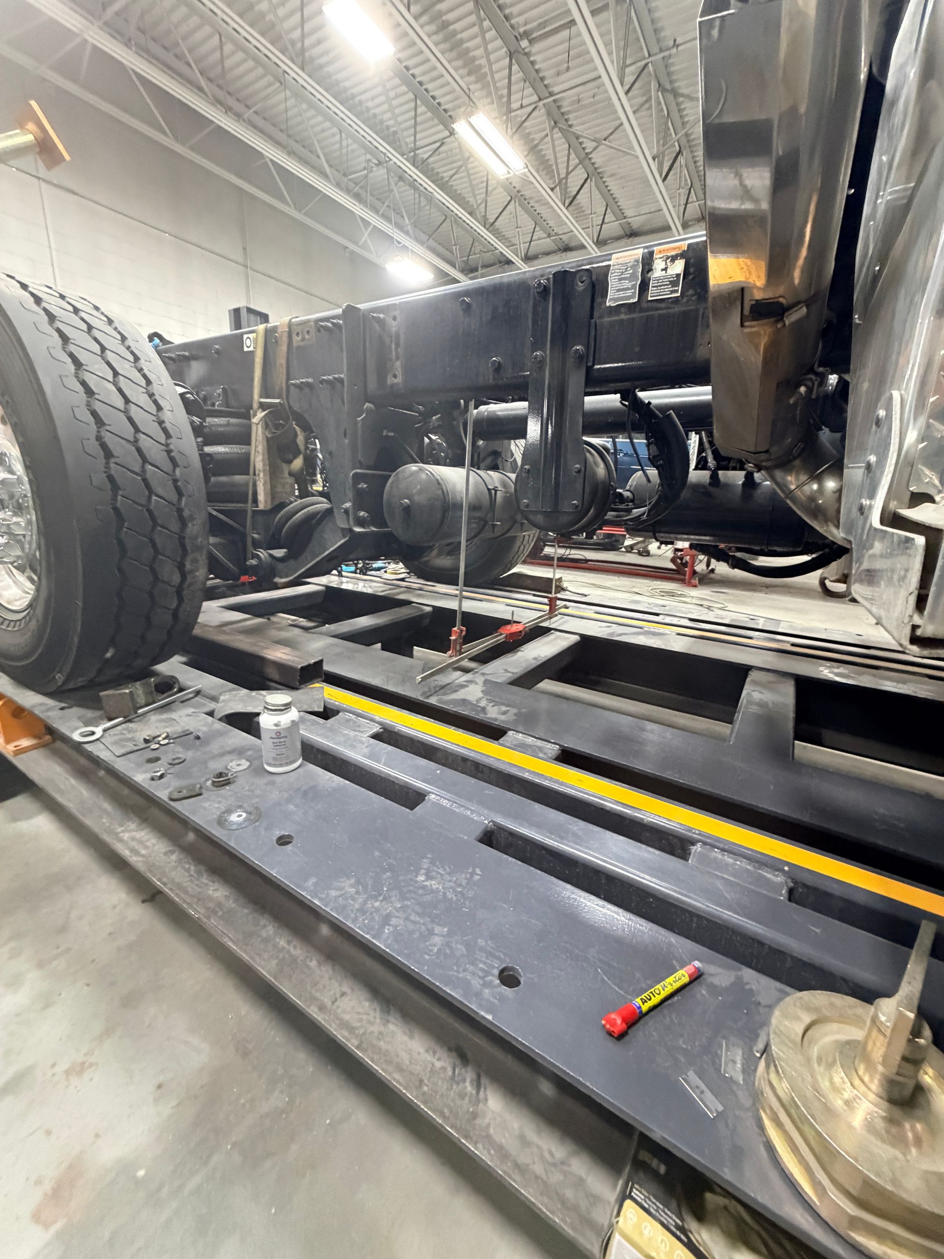 A semi-truck chassis undergoing maintenance on a shop floor lift.