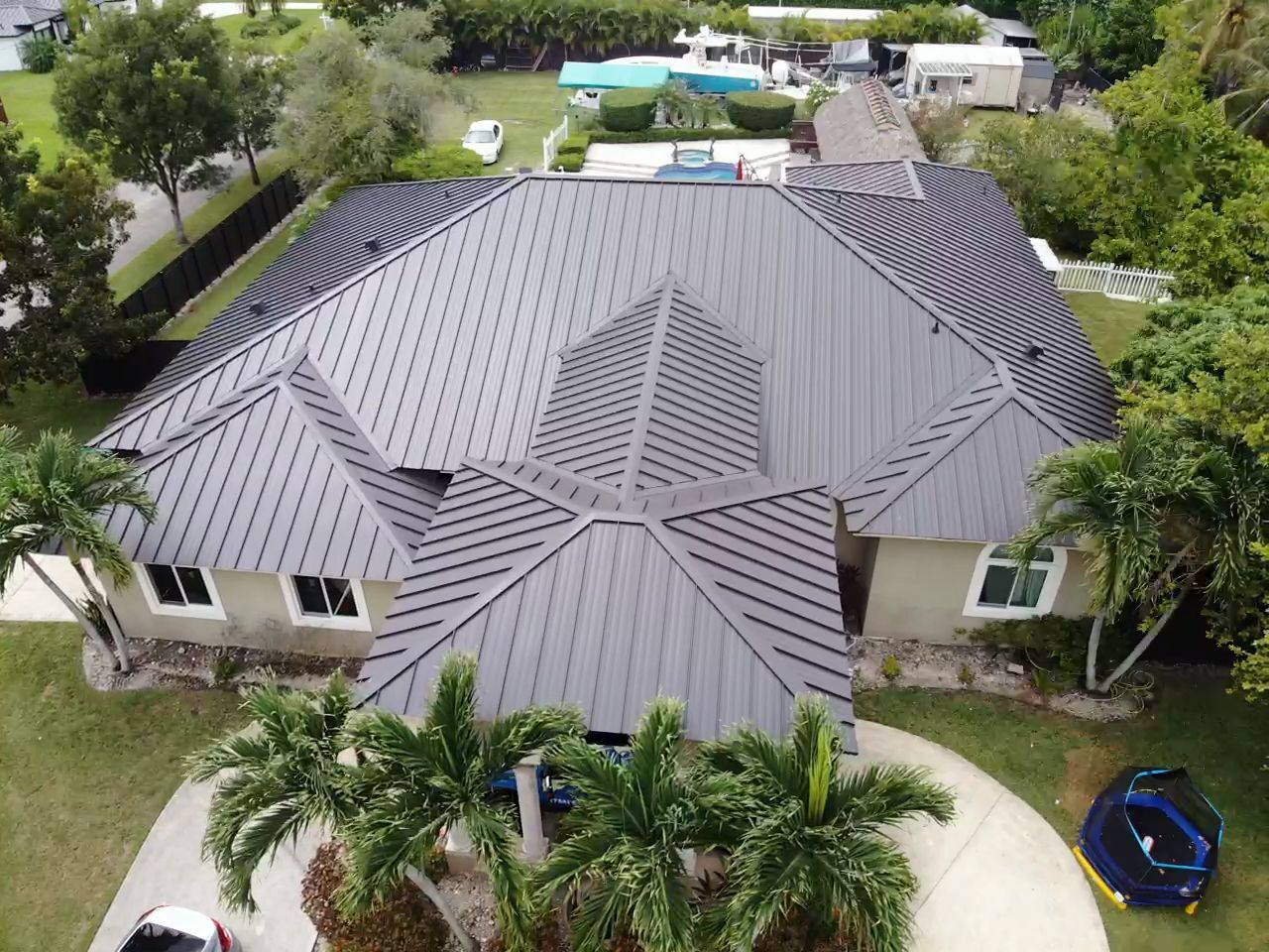 An aerial view of a house with a black roof surrounded by palm trees.