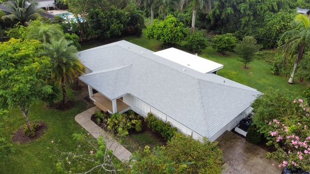 An aerial view of a house with a white roof surrounded by trees.